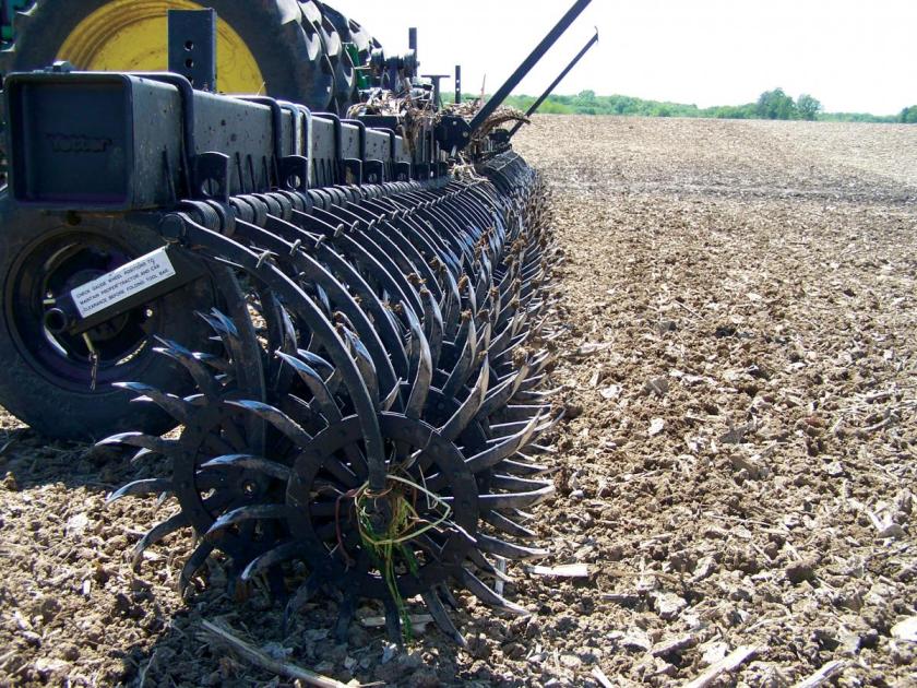Close-up of a farming implement with spiked metal wheels, showing details of its structure on a freshly plowed field.