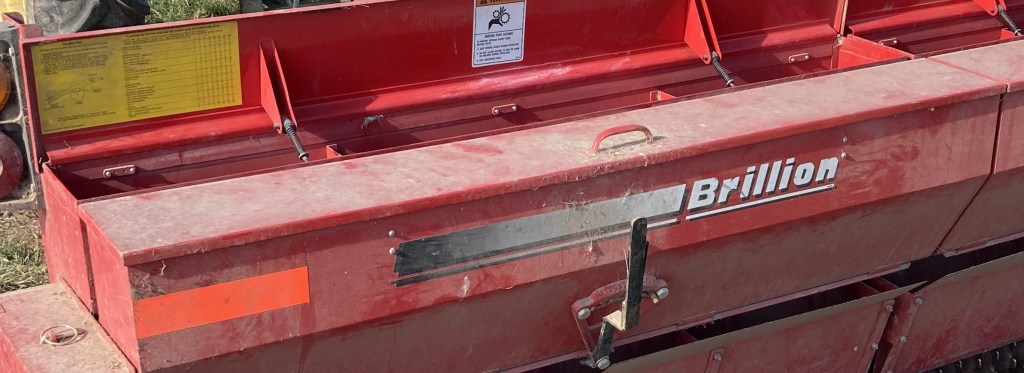 Close-up of a red Brillion agriculture equipment with visible warning labels and operational controls.